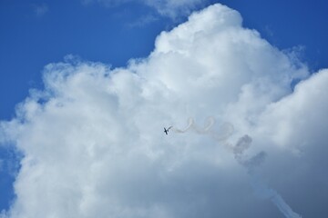 Aerobatic airplane performing spiral maneuver with smoke trail against bright blue sky and towering...