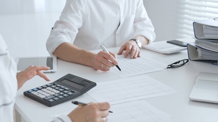 Two accountants collaborating in a well lit office, analyzing financial data and preparing reports with calculators and pens. Audit and taxes in business