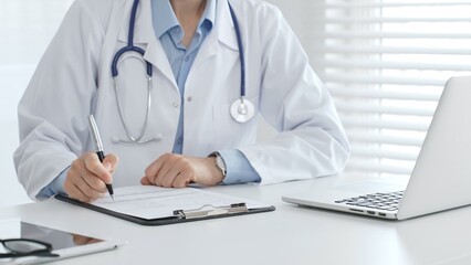 Female doctor documents patient information while working with digital devices at workplace in...