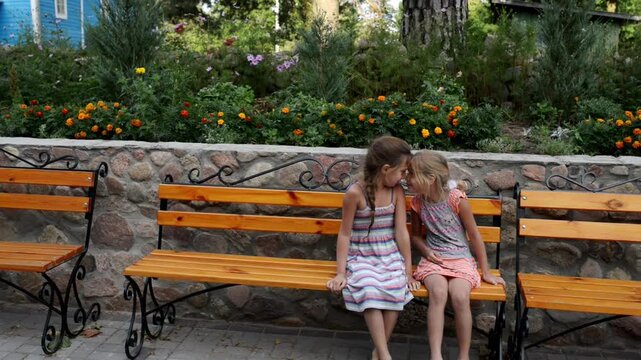 Two little girls are sitting on wooden bench near Orthodox church