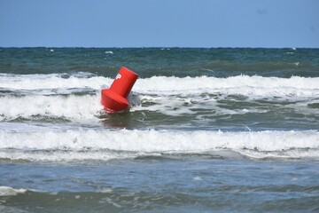 Red navigation buoy rocking in the surf along the shoreline.