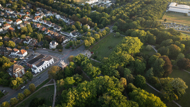 Aerial view of a suburban neighborhood with residential houses, tree-lined streets, and a large green park area, captured in warm evening light.