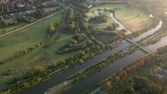 Aerial panoramic view of a river meandering through green fields and rural landscapes in Germany during sunrise, captured by drone.