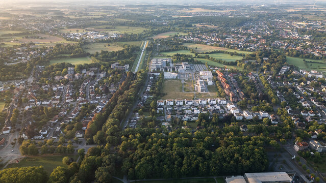 Aerial view of a suburban area with residential houses, green fields, and a canal at sunrise, captured by drone.