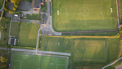 Aerial drone view of a sports complex with multiple football fields, running tracks, and green areas located along a canal.