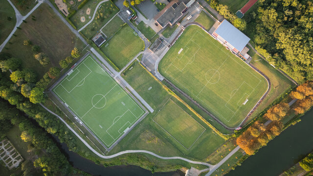 Aerial drone view of a sports complex with multiple football fields, running tracks, and green areas located along a canal. - Powered by Adobe