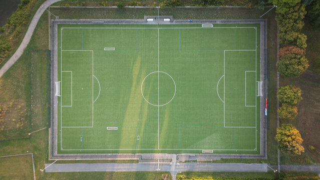 Aerial top-down view of a football field with green artificial turf and clear markings, sports infrastructure on a sunny summer day.