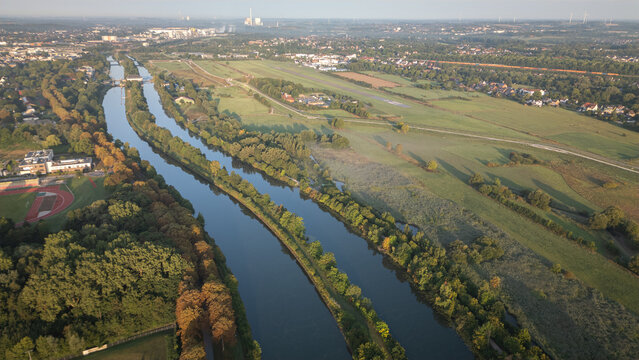 Aerial panoramic view of a river meandering through green fields and rural landscapes in Germany during sunrise, captured by drone. - Powered by Adobe