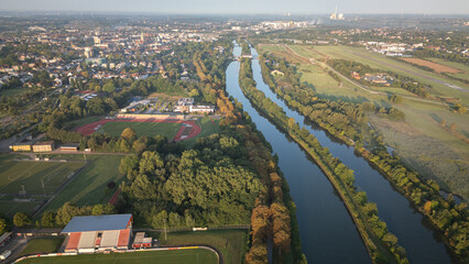 Aerial panoramic view of a river meandering through green fields and rural landscapes in Germany during sunrise, captured by drone.