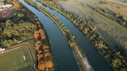Aerial panoramic view of a river meandering through green fields and rural landscapes in Germany during sunrise, captured by drone.