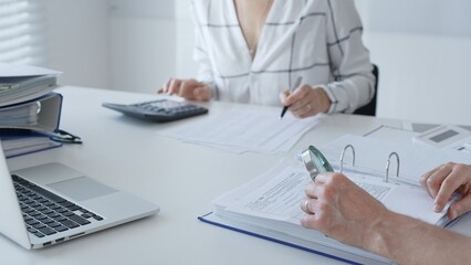 Team of professional accountants working together, using a magnifying glass and a calculators, to audit financial reports in their brightly lit office. Audit and taxes in business
