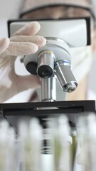 Close up of white gloved hand of a scientist adjusting a microscope in a laboratory. Medicine, health care and science concept