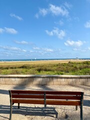 Obraz premium Wooden bench facing the sandy beach and Mediterranean Sea in Vilanova i la Geltrú, Catalonia, Spain, under a bright blue sky.