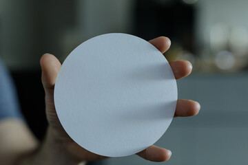 Close-up of a hand holding a plain, round white disc. Perfect for presentations or mockups.