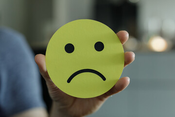 A hand holding a sad face emoticon.  Perfect for illustrating negative emotions, unhappiness, or disappointment.