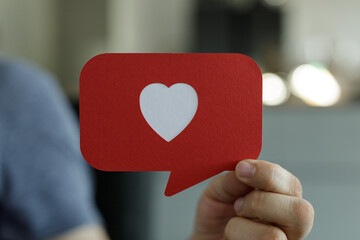 Person holding a red speech bubble with a white heart.  Perfect for social media, love, and positive emotions.