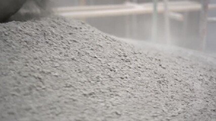 A sizable mound of gray powder or particulate matter filling the frame with a slight dusting effect and blurry industrial equipment visible in the background - Powered by Adobe