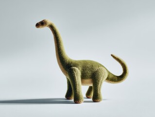 A stuffed, long-necked dinosaur toy, green body, long neck, tail curled, on a light backdrop