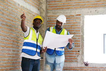 A young male engineer carries structural blueprints and a laptop while inspecting work at the construction site.