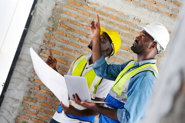 A young male engineer carries structural blueprints and a laptop while inspecting work at the construction site.