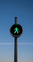 Green pedestrian signal showing a walking man symbol against a clear blue sky