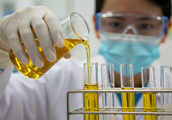 Lab technician conducting a chemical experiment with yellow fluid. A scientist in protective gear carefully pours a solution into glassware, symbolizing pharmaceutical research, quality control