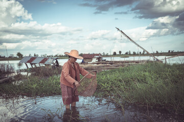 Young Fisherman in Traditional Attire Engaging in Fishing Activity on a Calm River Under a Dramatic Sky Surrounded by Nature