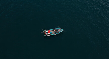 Fototapeta premium A solitary fishing boat floats peacefully on the deep, dark blue sea, captured from an aerial perspective.