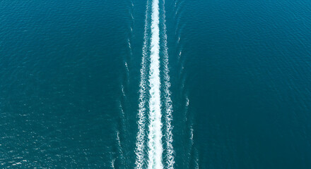 An aerial top-down view of a motorboat's white wake trail on the deep blue sea.