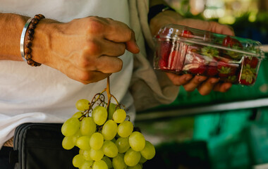 Close up of hand with a grape and berry in plastic box on the local Farmers market. Shopping At Farmers Market Stall. Close up. Part of the series