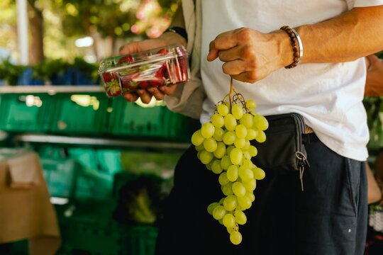 Close up of hand with a grape and berry in plastic box on the local Farmers market. Shopping At Farmers Market Stall. Close up. Part of the series - Powered by Adobe