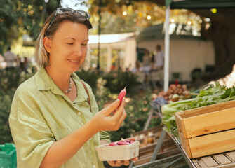 Close up of hand with a radish in shopping basket on the local Farmers market. Mature Female Customer Shopping At Farmers Market Stall. Close up. Part of the series