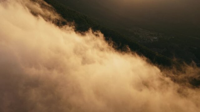 Drone video of mountain peaks surrounded by golden clouds at sunset, with warm light illuminating the misty slopes in Spain.