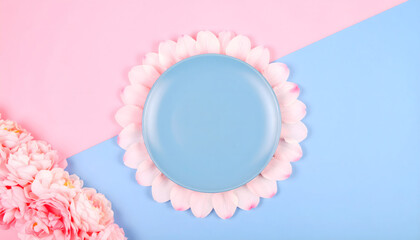 Pastel flat lay with a blue circular podium on a pink petal frame against a split pink and blue background.