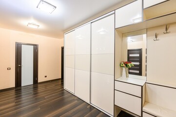 modern hallway featuring a large white sliding door closet, dark wood floors, and a beige color scheme, lit by recessed ceiling lights