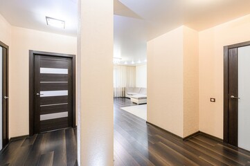 Interior shot of a hallway with dark wood floors, beige walls, and two dark doors. A glimpse into a living room reveals a sofa and chandelier