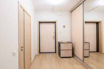 well-lit hallway with light wood floors, white walls, and various doors, including a mirrored closet