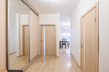 Bright hallway with wooden floors, doors, and a mirrored closet.  A dining table is visible in the background