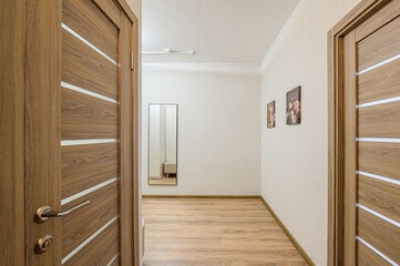 Hallway view with wooden doors, light patterned wallpaper, wooden floor, mirror, and pictures on the wall