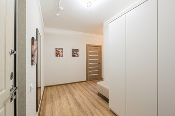 well-lit hallway with wood floors features a white wardrobe, artwork, and a wooden door