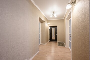 well-lit hallway features textured beige wallpaper, light wood floors, and a dark entry door framed by white molding