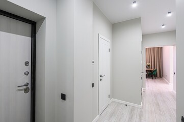 Hallway view with doors and a glimpse of a room with a table, flowers, and chairs, all in light, neutral tones