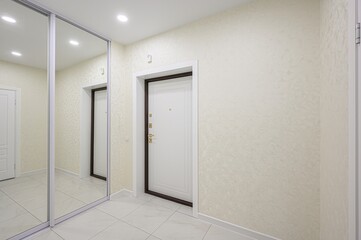Bright, modern hallway with a sliding mirrored wardrobe, white doors, and textured light beige wallpaper. Tiled floor and recessed lighting