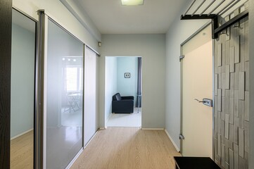 well-lit hallway with light blue walls, wooden floor, and glass sliding doors leading to other rooms. A door with a unique textured design is on the right