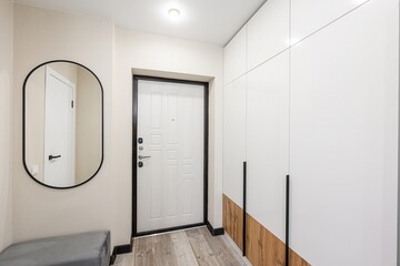 bright entryway with a white front door, wardrobe, and a round-edged mirror