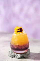 Lavender syrup and orange soda cocktail in a glass with crumbled ice on a lilac background