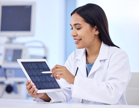 A female doctor in a lab coat examining medical scans on a digital tablet with a stylus in a clinic.
