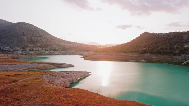 Drone video capturing a serene mountain lake in Spain at sunset, with golden light reflecting on turquoise waters and rugged hills in the background.