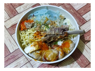 Bakso. A bowl of rib meatballs with yellow noodles, blue vermicelli, shredded cabbage, fried onions and chili sauce on a wooden patterned table. The meatballs look very delicious and delicious.