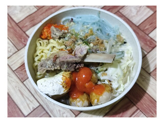 Bakso. A bowl of rib meatballs with yellow noodles, blue vermicelli, shredded cabbage, fried onions and chili sauce on a wooden patterned table. The meatballs look very delicious and delicious.
